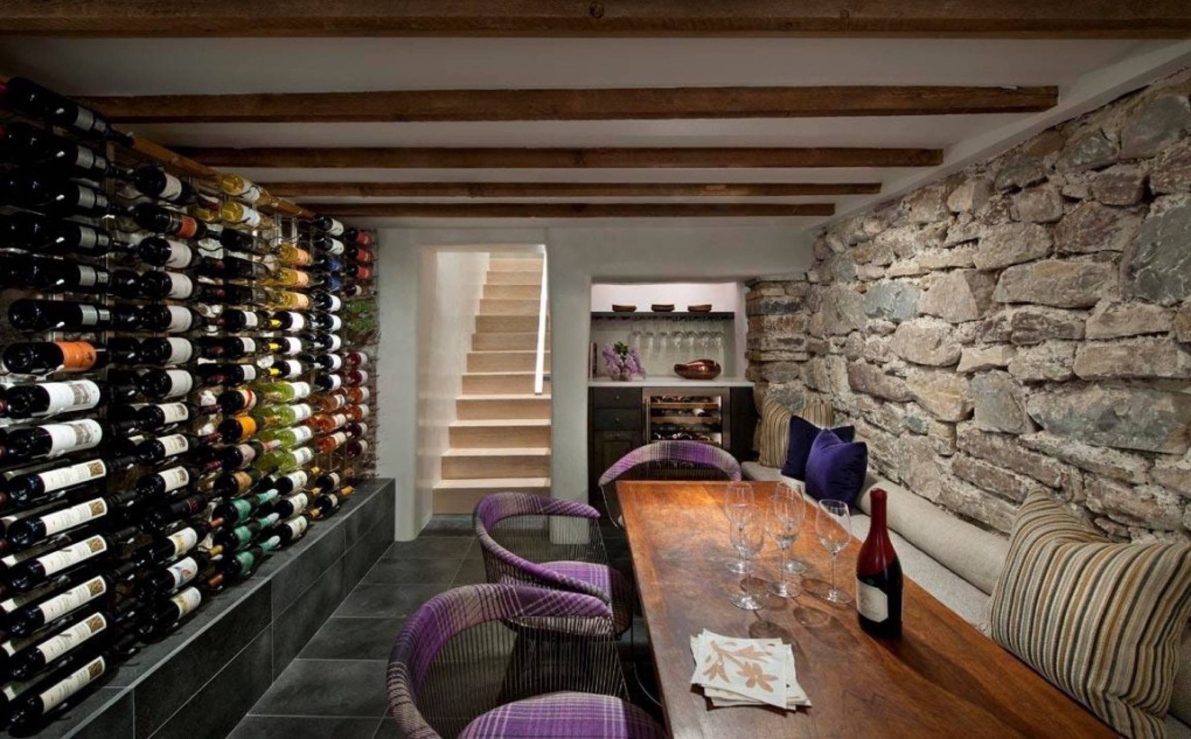 Stylish basement wine cellar with private staircase access, wine racks, seating area, and mini-fridge